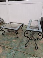 Photo showing both tables on outdoor tiled surface against a white fence. The coffee table is square, and the buffet table is rectangular with wrought iron styled legs, clear glass tops surrounded by blue-gray waterproof tile.