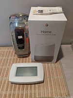 Photo showing three items on a table: sealed Google Home speaker, sealed Monster Power Appliance PowerCenter 200, and a white Honeywell thermostat controller.