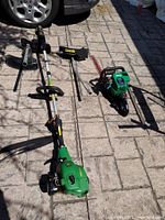 Wide shot showing John Deere powerhead, three detachable heads, and Weed Eater Excalibur hedge trimmer on patio
