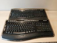 Top view of two Microsoft Wireless Laser Keyboard 7000 keyboards stacked, showing layout and ergonomic split key design with media keys on top row.