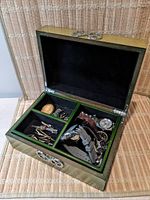 Green wooden jewelry box open with removable top tray displaying compartments of tie clips, earrings, and watches