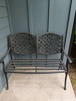Front view of two-seater metal bench with floral backrest and slatted seat