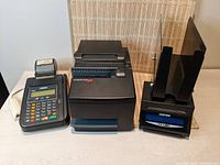 Front view showing the Hypercom T7Plus card processing unit (left) with keypad and small receipt printer, CognitiveTPG large receipt printer (middle) with front paper slot, and Custom TK180 printer with dual upright paper holders (right).