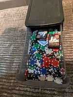 Box drawer filled with scattered poker chips in blue, green, red, and white colors. Two decks of playing cards on top in unopened packaging.