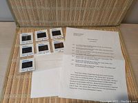 Photo of all 7 mounted 35mm slides and a single-page color caption and production summary sheet, arranged on fabric surface