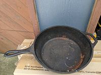 Top view showing the round deep cast iron pan with some surface rust inside, long handle, and two side handles.