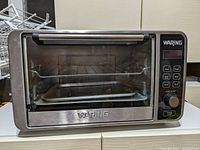Front view of Waring TCO650 Pro digital convection oven showing glass door, stainless steel body, control panel with buttons and knob, oven rack, and tray inside.