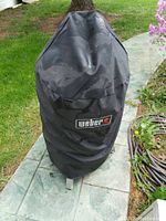 Smoker covered with black Weber-branded cover on patio