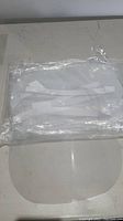 Photo showing a sealed plastic bag containing multiple clear face shields with white elastic straps inside.