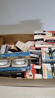 Box containing assorted light bulbs of various brands and types in retail packaging, and loose bulbs.