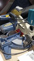 Full side view of Ryobi 10 inch miter saw showing the cracked frame, motor, and handle with trigger.