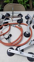 Photo showing multiple suction cups with metal frames and rubber cups, along with orange pressure hoses and valve gauge on a table outdoors.