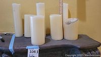 Eight white battery operated candles on a wooden surface, some with slightly melted tops, one showing discoloration or damage at the top.
