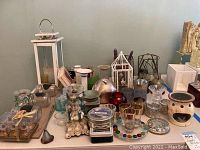 Wide view of various candle holders including lanterns, ceramic, metal and glass holders arranged on table