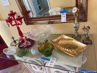 Wide photo of entire lot with red glass candelabra, decorative bowls, clock, figurine, and ashtray on glass table below mirror