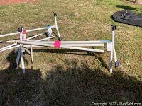 Photo of white metal clothes rack frame with caster wheels lying on grass, partially assembled or disassembled.