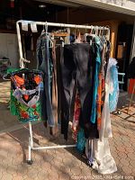 Full view of white metal rolling rack with horizontal bar holding assorted clothing (not included)