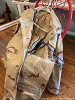Desert camouflage jacket hanging on a red metal rack, showing front pocket and button details.