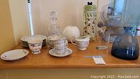 Wide view of the ceramic plates, tea cups, saucers, child's head cup, and glass decanter placed on wooden table.