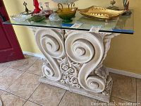 View of entry table with glass top and two decorative carved stone pedestals showing overall design and condition