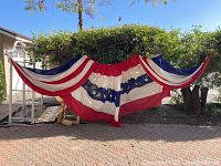 Full view of large red, white, and blue decorative fabric flag deployed outdoors.
