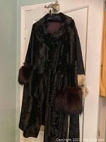 Front view of the black Borella fur coat hanging on a door showing the large fur cuffs in brown and beige.