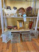 Full view of shelf showing all glass pieces, ceramic planter, figurines, gold frame, vases, and bowls.