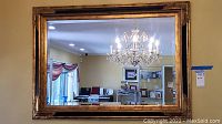 Frontal view of the 43x31 beveled mirror with ornate golden frame reflecting a chandelier and interior room.