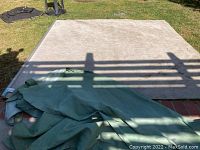 Beige outdoor roll shade spread out on the ground with rolled green fabric curtain, showing size and condition.