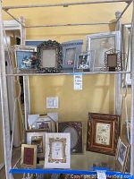 Multiple picture frames displayed on metal shelving, varied sizes and decorative styles.