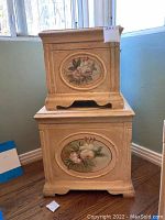Photo of two stacked shabby chic decorative wooden boxes with floral oval painted panels, beige distressed finish, carved bases and storage compartments