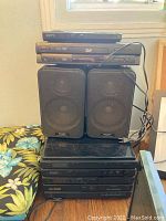 Sony, Shinsonic DVD players stacked with Shinsonic bookshelf speakers and Sharp stereo components below on a shelf.