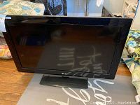 Front view of LG TV showing the black screen, black bezel, and stand base on wooden floor.