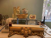 Overview photo showing porcelain vase, ornate gold decorative shelf/frame, wicker basket, blue and white shelves, small framed photo, metal and acrylic stands.