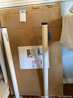 Photo showing large cardboard box with two white table legs and a printed sheet attached to the box.