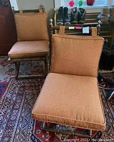 Front view of two bamboo chairs with orange cushions on a patterned rug.