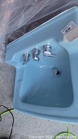 Photo showing powder blue ceramic sink with chrome faucet hardware from top and side angles.