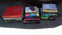 Three piles of books on pavement, showing a mix of fiction and non-fiction titles, both hardback and paperback.