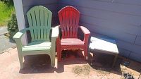Photo of two outdoor Adirondack-style chairs, one green and one red, sitting on a patio beside a small stone top table with wood base.