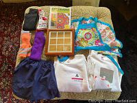 Lot items displayed on a bed showing the clothing, apron, coloring book, tic-tac-toe game, and socks organized.