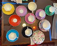 Overhead view of colorful bone china tea cup sets and separate tea plates on dark surface, showing multiple cup and saucer pairs in various pastel and bright colors