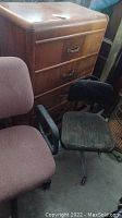 Four drawer wood dresser with metal handles, vintage black fabric office chair with armrests and caster wheels, mauve fabric adjustable office chair with plastic armrests.
