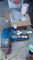 Box containing multiple light fixtures and parts including an outdoor lantern-style sconce, chrome and brushed metal sconces with frosted glass shades, mounting bars, and packaging materials.