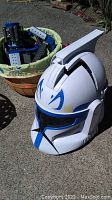 Photo of white Star Wars Clone Trooper helmet with blue markings beside wicker basket filled with Lego pieces.
