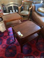 Pair of wooden end tables placed on a patterned rug near armchairs, showing front and top of tables.
