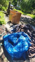 Photo showing wooden vanity cabinet and blue and brown tarps outdoors in sunny garden setting.