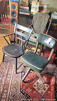 Two vintage chairs: one wooden with green upholstery and castors, the other black painted wood with armrests.