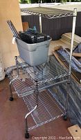 Large assembled metal wire shelving unit with 4 caster wheels, shown with plastic tub and unassembled parts on lower shelves.
