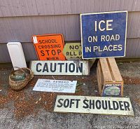 Overview of lot showing multiple vintage traffic and caution signs, wooden crate, basket with bottles, porcelain cover, and reward paper sign placed outside against building
