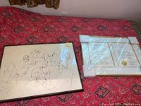 Overview of the two framed items placed on a red patterned cloth, showing the art sketch and framed certificate side by side.